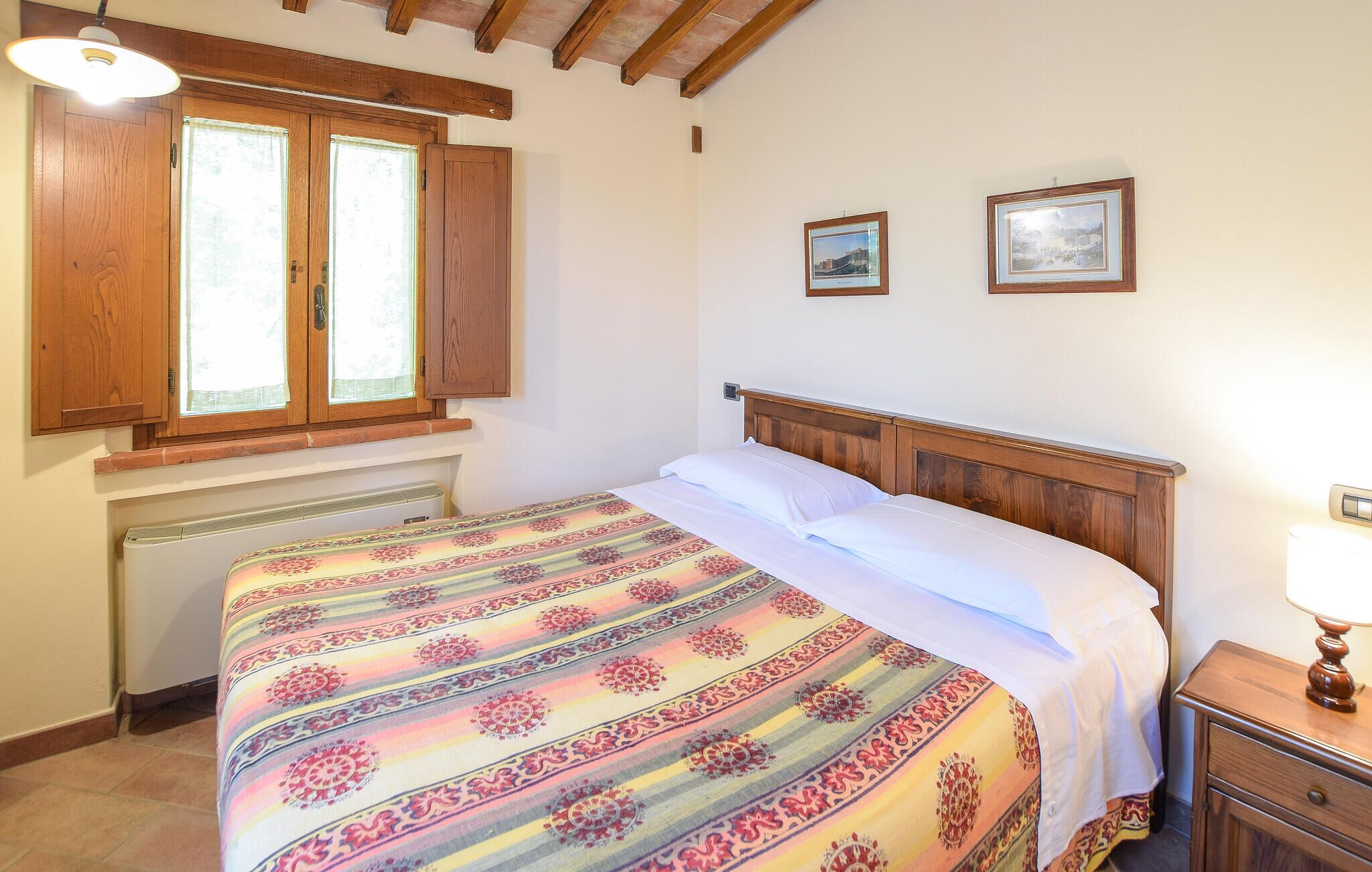 A bedroom with a wooden bed, a window with wooden shutters, a radiator, and two framed pictures on the wall.