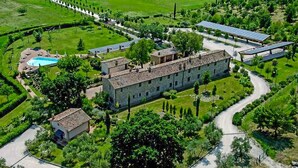 Vue aérienne d’un vaste domaine comprenant un bâtiment central en pierre, une piscine et des panneaux solaires.