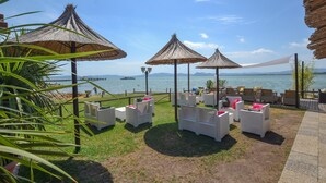 Un espace aménagé près de la plage, avec des parasols en chaume, des meubles en osier et une vue sur la mer.