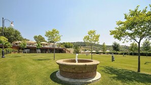 Une fontaine située dans une structure circulaire en briques, entourée de pelouse, avec un bâtiment en arrière-plan.