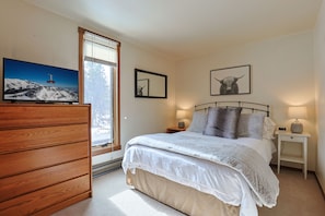 Une chambre à coucher avec un lit, des tables de chevet, une télévision et une fenêtre avec des stores.