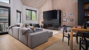 A modern living room with a large gray sectional sofa, a flat-screen TV, a fireplace, and a dining area with a wooden table and chairs.