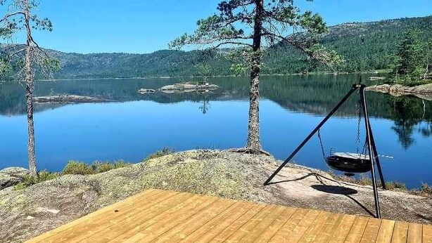En træterrasse ved en rolig sø med en gyngestol.
