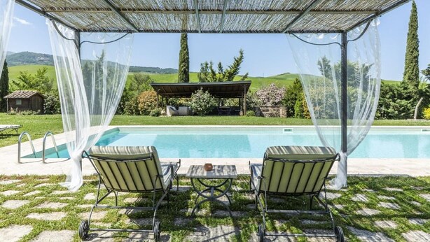 A covered outdoor area with a pool, two lounge chairs, and a table.