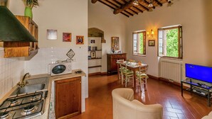 Una cocina con estufa, pileta y alacenas de madera. Cuenta con una zona de comedor con mesa y sillas, y un televisor.