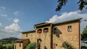 Un edificio de piedra con techo de tejas, ventanas de arco y plantas en macetas en el patio.