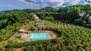 Una gran piscina rodeada de exuberante vegetación y un viñedo, con un edificio de piedra al fondo.