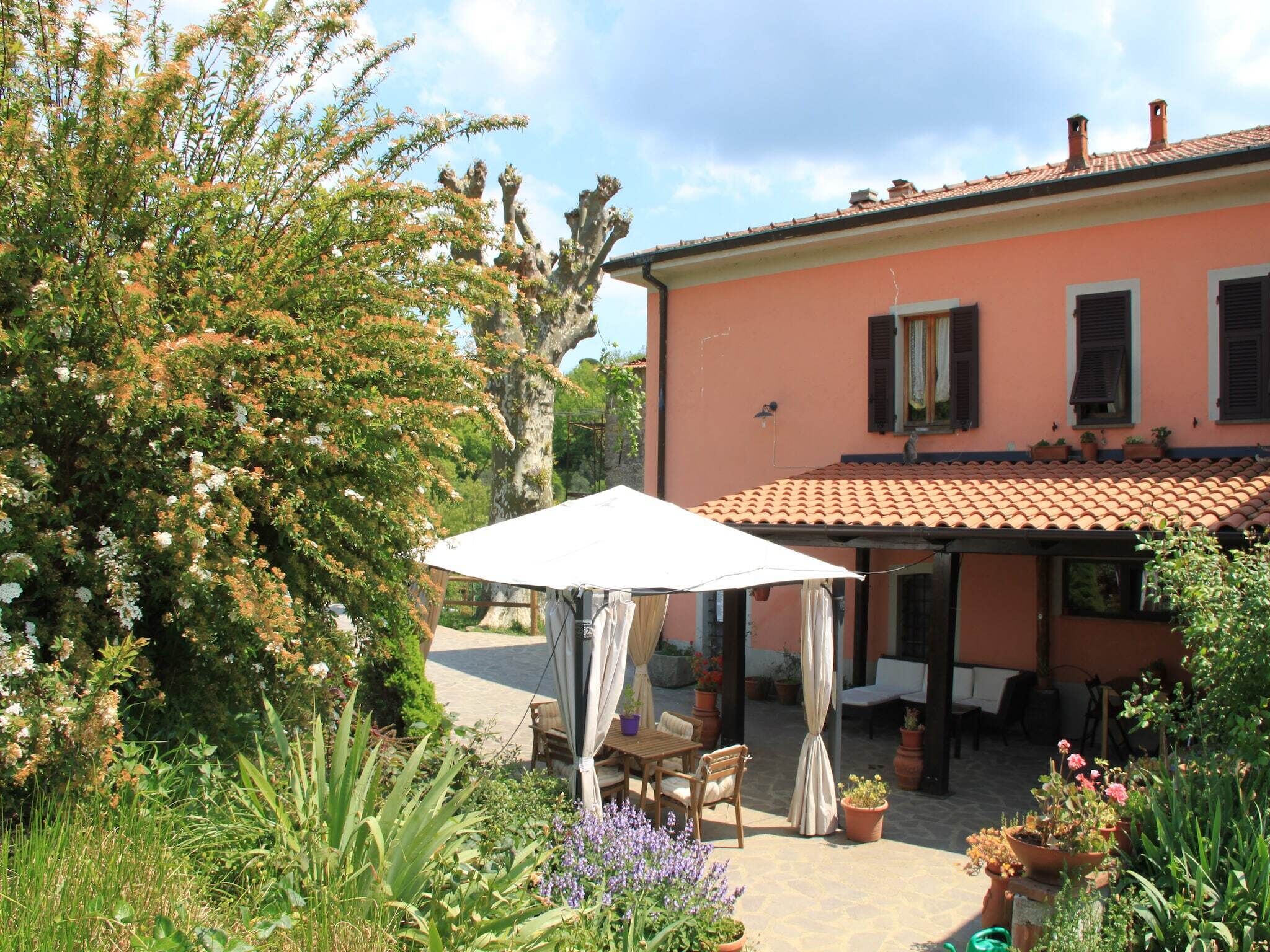 Une maison avec un toit en tuiles et un jardin comprenant une table et des chaises sous un parasol blanc.