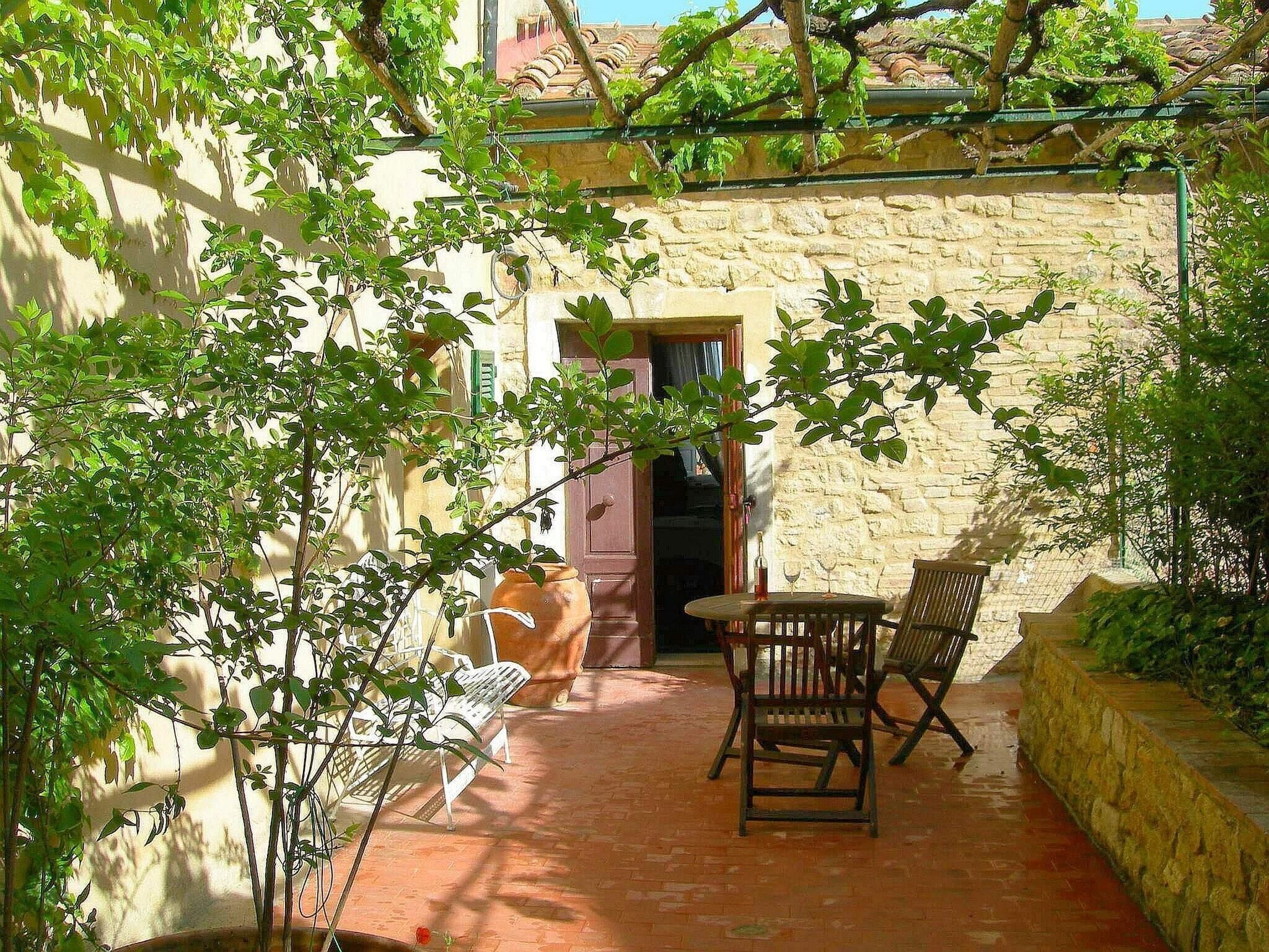 A rustic outdoor patio with a stone wall, a wooden table, two wooden chairs, and a potted plant.