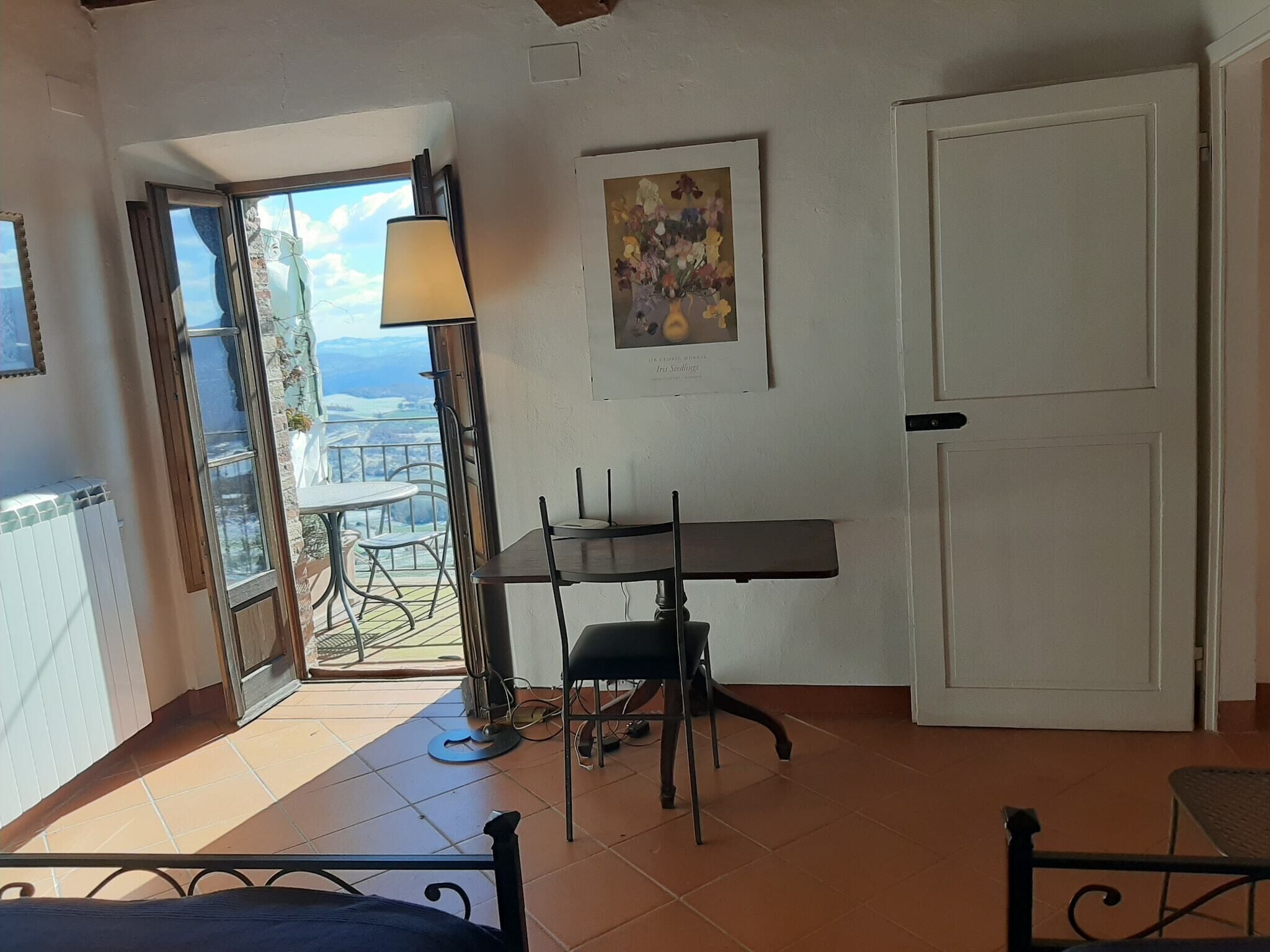 Quarto com varanda, mesa de jantar com cadeiras, luminária e porta.