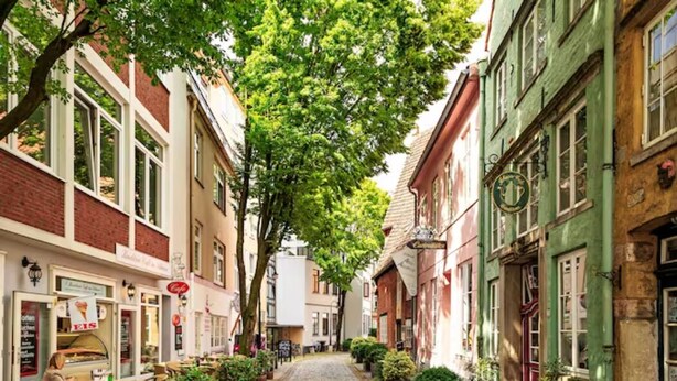A cobblestone street lined with historic buildings, outdoor seating for cafes, and potted plants. - 4-room residence for families and groups with balcony and garden view! (Leipzig)