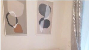 A living room with a beige sofa, two cushions, a small white coffee table, and abstract art on the wall. - 4-room residence for families and groups with balcony and garden view! (Leipzig)