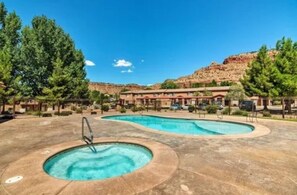A pool area with a hot tub, surrounded by trees and a building with multiple windows. - Red Rock Adventure Stop (Kanab)