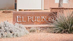 Een bord met de tekst 'EL PUEBLO' in een woestijnlandschap met schaarse begroeiing.