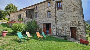 A stone building with a sloped roof, a small porch, and a grassy yard with colorful chairs.