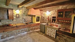 A rustic kitchen with stone walls, wooden beams, and a stone floor.