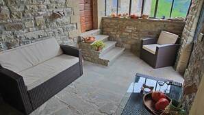 Eine Terrasse mit Steinwänden, Korbmöbeln, einem Glastisch und Blick auf die Landschaft.