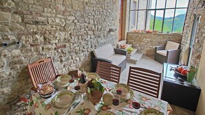 Ein rustikaler Essbereich mit Steinsandsteinwänden, ein gedeckter Tisch, Korbmöbel und Blick ins Freie.