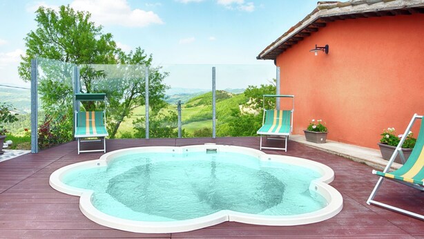 Une piscine sur le toit, dotée de deux chaises longues, d’un espace clos en verre et offrant une vue sur des collines verdoyantes.