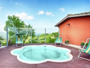 Ein Dachpool mit zwei Liegestühlen, einer Glaskonstruktion und Blick auf grüne Hügel.
