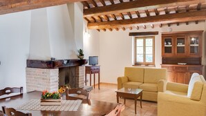 Un salon chaleureux avec une cheminée, des poutres apparentes, un canapé et un coin repas comprenant une table et des chaises.