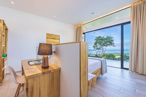 A bedroom with a large window, a desk with a lamp, a bed, and a view of the outdoors. - Luxury Villa Elegante - Ocean View 4 Bedroom House (Savegre)