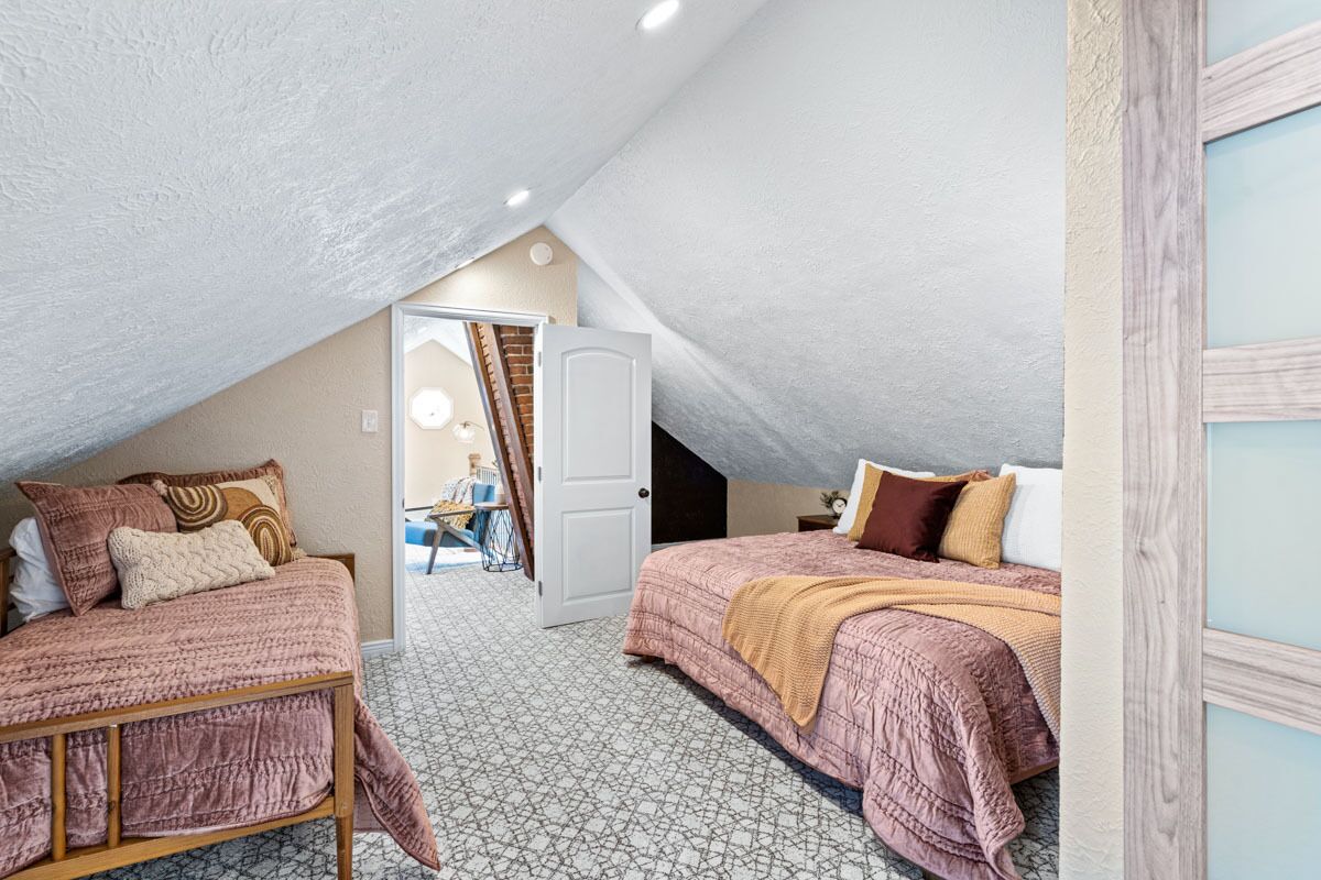 A bedroom with two beds, a sloped ceiling, and a door leading to another room.