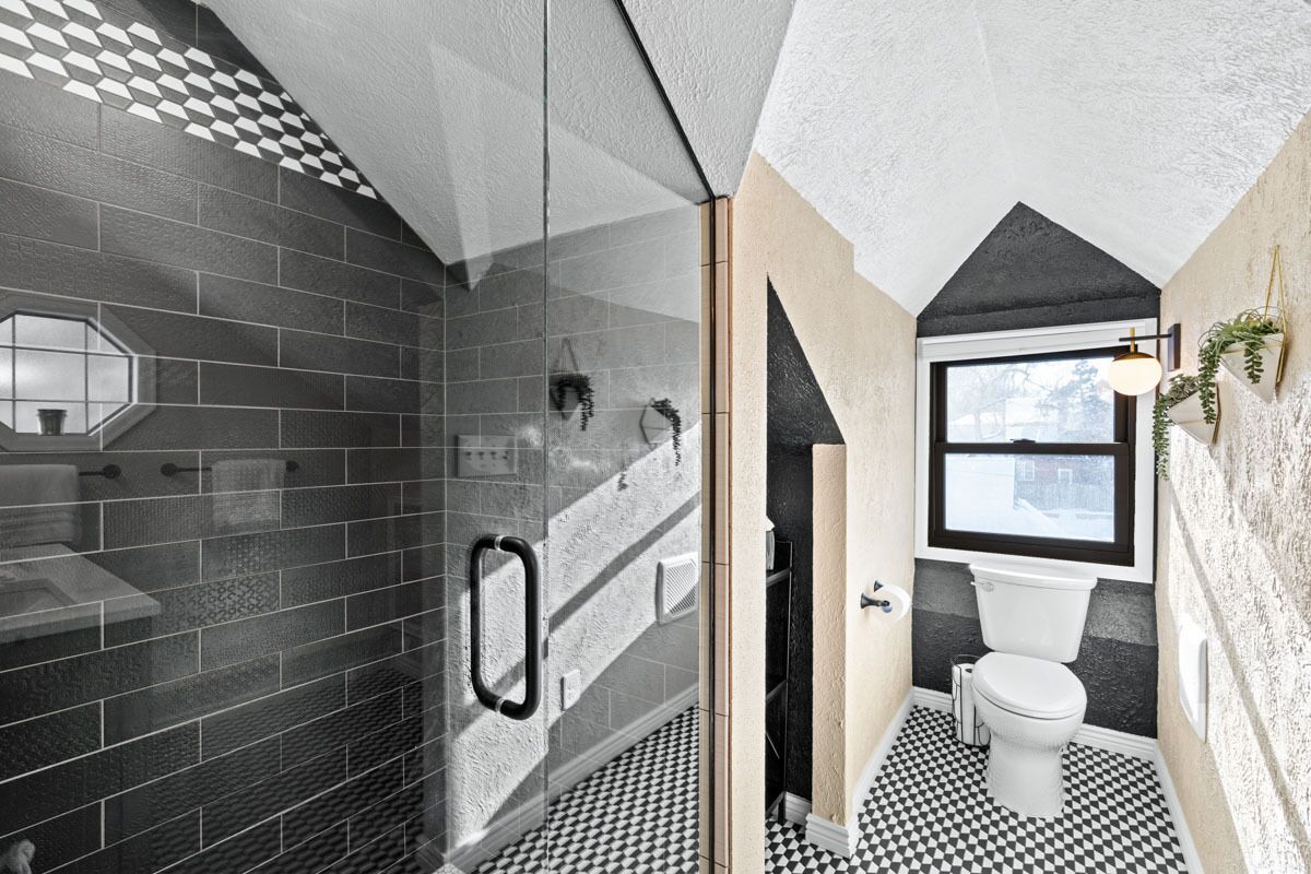 A modern bathroom with a checkered floor, a glass shower enclosure, and a window with a view.