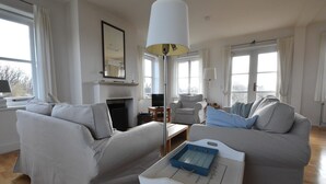 A modern living room with two sofas, a coffee table, a fireplace, and large windows. - Villa in Midsland near the Sea (Midsland Terschelling)