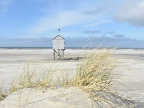 Eine Strandhütte mit schlichtem Design, gelegen an einem sandigen Strand mit Dünen im Vordergrund.