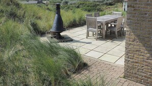 A patio with a table and chairs, a chimney, and a view of houses in the distance. - Villa in Midsland near the Sea (Midsland Terschelling)