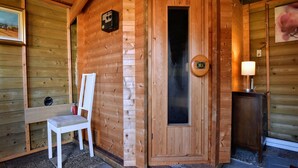Una sauna in legno con una panca, una porta e un piccolo tavolo con una lampada.