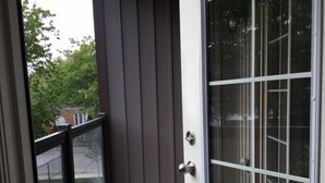 A balcony with a wooden floor, metal railings, and a glass door leading to a room.