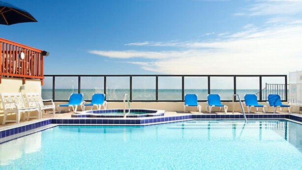 Zona de piscina con sillas azules y un jacuzzi, con vistas al océano.