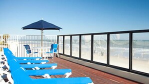 Terraza con sillones azules y una sombrilla grande, con vista a la playa.