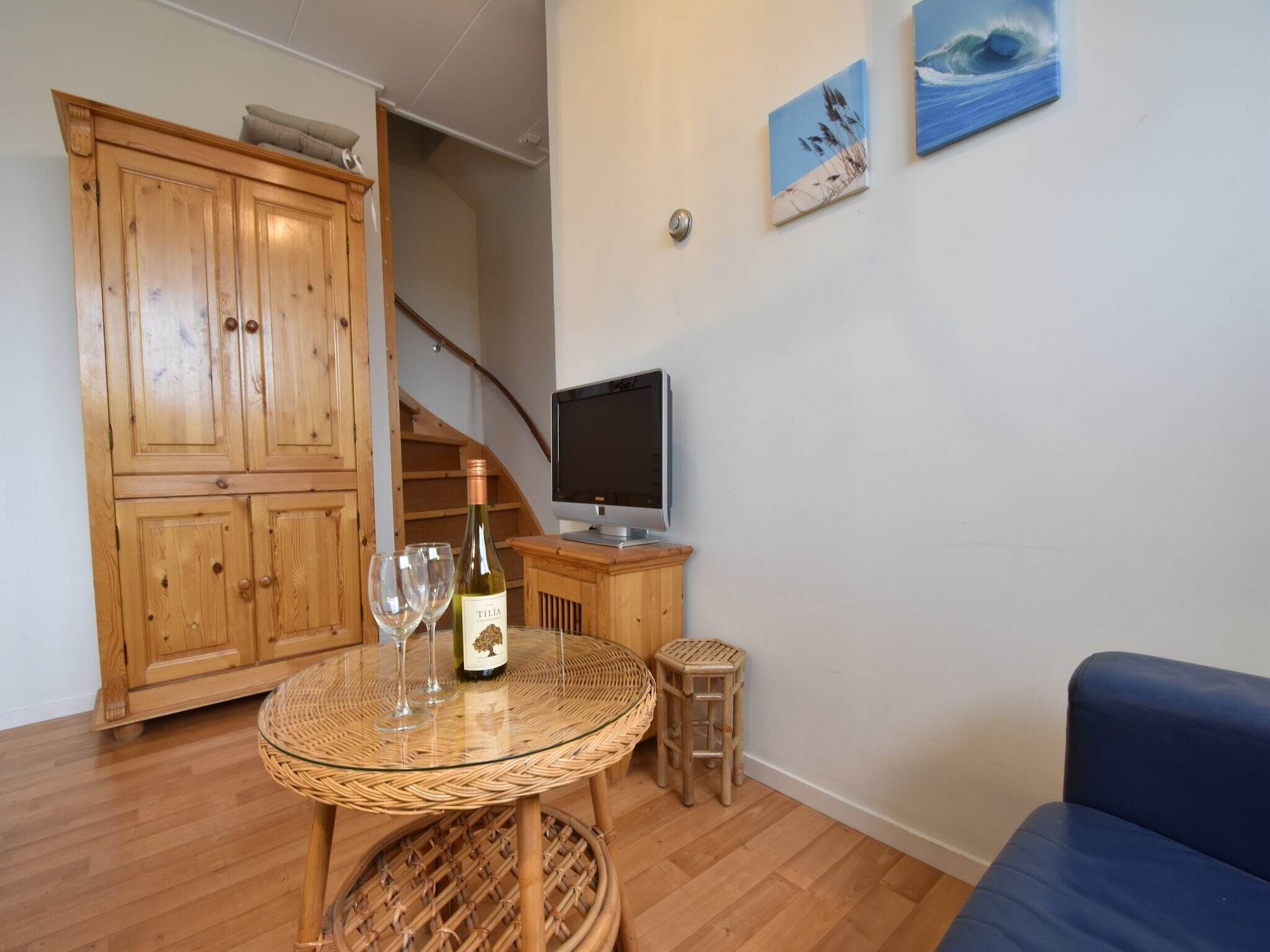 Una sala de estar con un aparador de madera, un televisor, una mesa de mimbre con copas de vino y un sofá azul.
