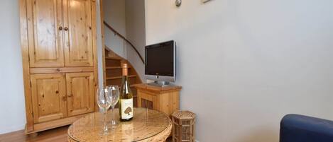Una sala de estar con un aparador de madera, un televisor, una mesa de mimbre con copas de vino y un sofá azul.