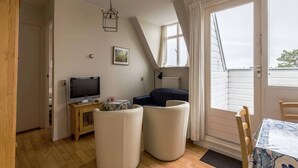 Une pièce confortable avec une télévision, une petite table, deux chaises, un canapé et une fenêtre avec des rideaux.