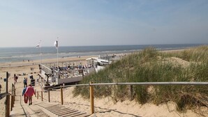 Une promenade en bord de mer qui mène à une plage de sable, avec un poste de surveillance des sauveteurs et une vue sur l’océan.