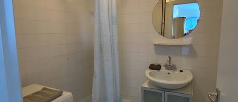 A bathroom with a shower, a washing machine, a sink, and a mirror.