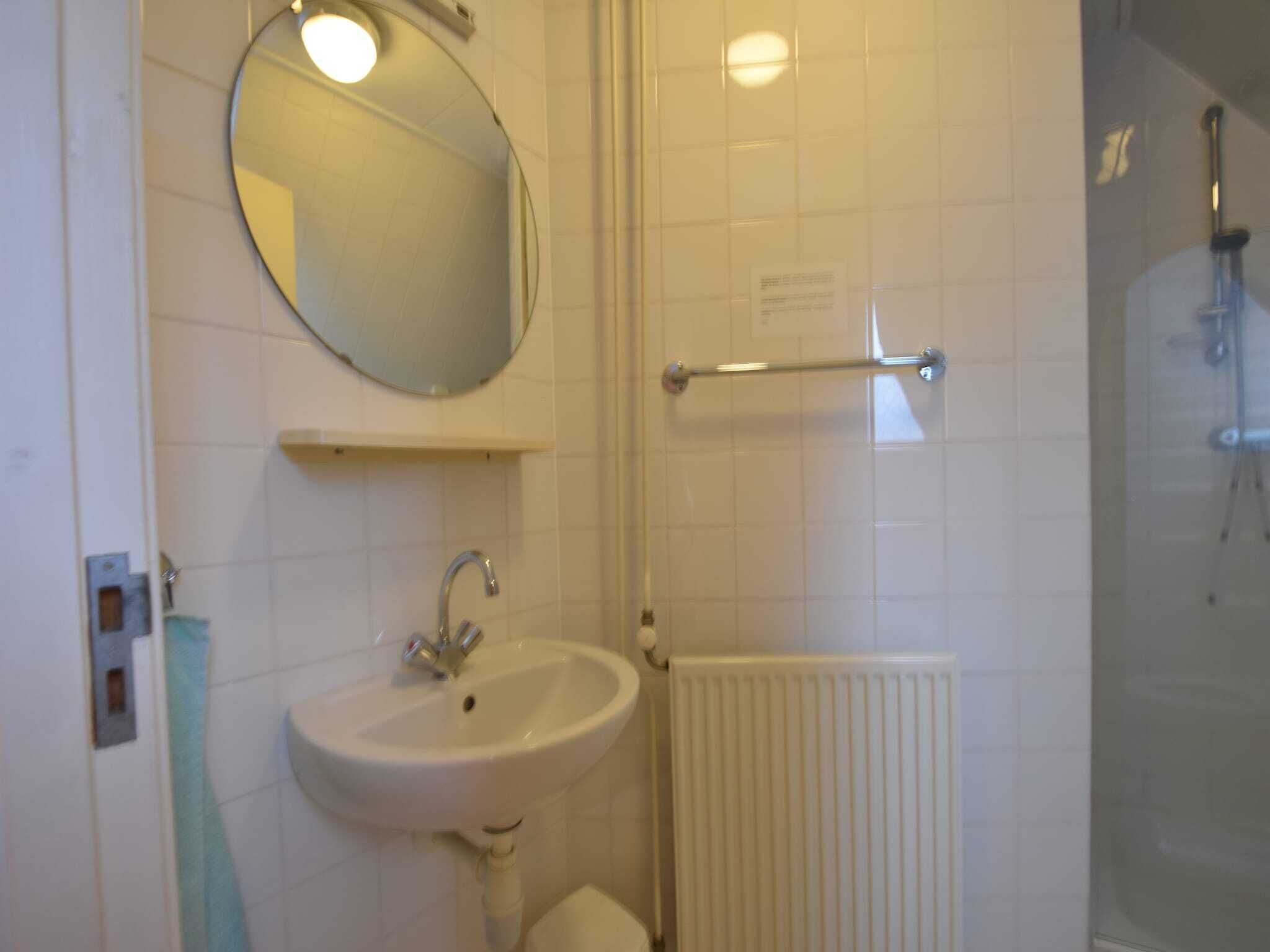 A bathroom with a white sink, a round mirror, a towel rack, and a shower area.