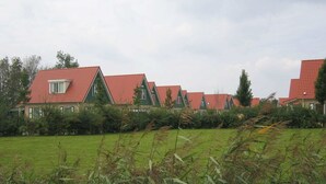 A row of houses with red roofs and green walls, surrounded by a grassy field and trees. - Holiday home near Grevelingen Lake (Zonnemaire)