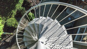 A spiral staircase with metal railings and perforated steps, surrounded by greenery.