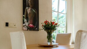 A dining area with a wooden table, white chairs, a vase with flowers, and a painting on the wall.