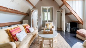 A cozy loft bedroom with exposed wooden beams, a large window, a sofa, a coffee table, and a TV. - Mansion in Deil by River Linge (Deil)
