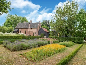 A traditional brick house with a sloped roof, surrounded by a well-maintained garden with various flower beds and hedges. - Mansion in Deil by River Linge (Deil)