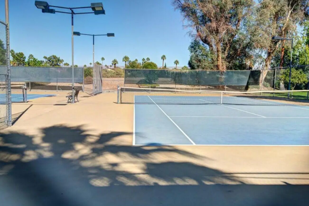 Un court de tennis en plein air, doté d’un filet, entouré d’une clôture et d’arbres.