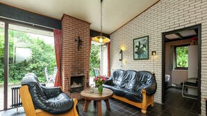A modern living room with a fireplace, leather sofas, a wooden coffee table, and a large window offering a view of greenery. - Lake Escape w/ Garden (Kamperland)