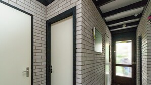 A hallway with white brick walls, a tiled floor, and a door with a black frame. - Lake Escape w/ Garden (Kamperland)