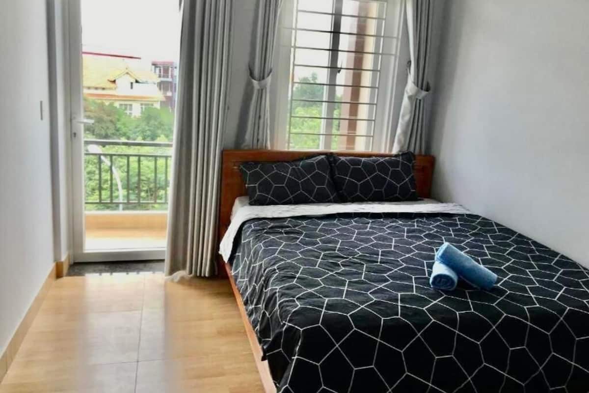 A bedroom with a bed, a window with curtains, and a view of a balcony.